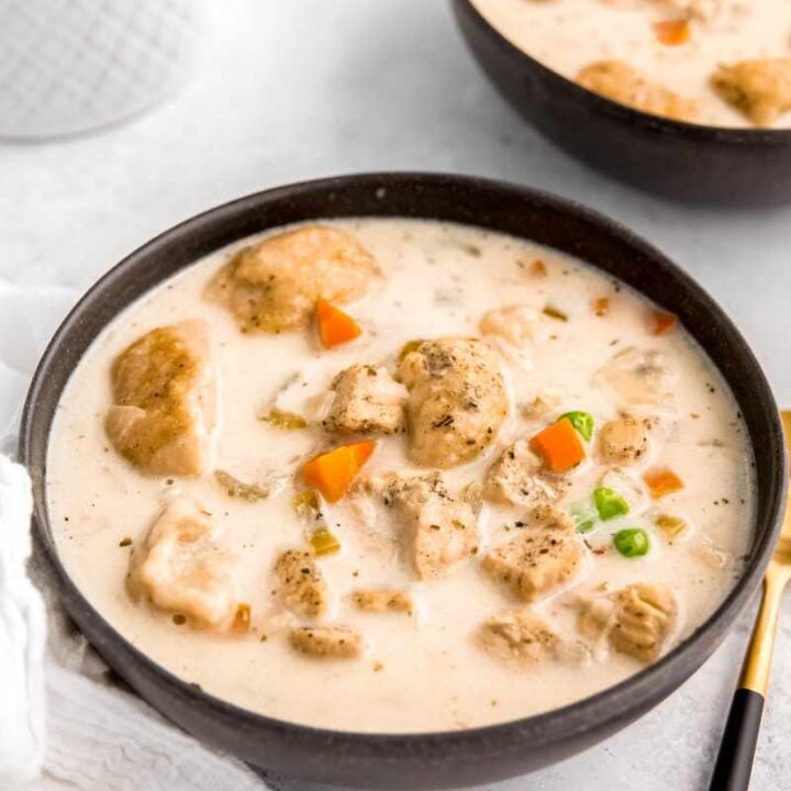 A dark serving bowl filled with creamy instant pot chicken and dumplings soup on a light background.